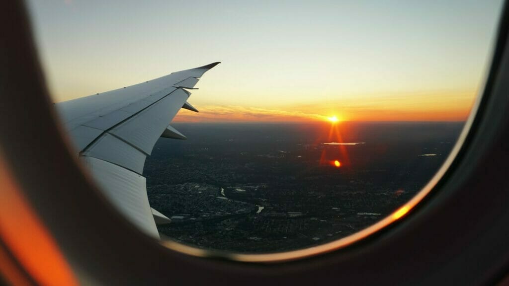 Das Foto zeigt den Blick aus einem Flugzeugfenster, man sieht den Flugzeugflügel und am Horizont die Sonne aufgehen. Das Auswandern aus Deutschland kann zur persönlichen Entwicklung beitragen.