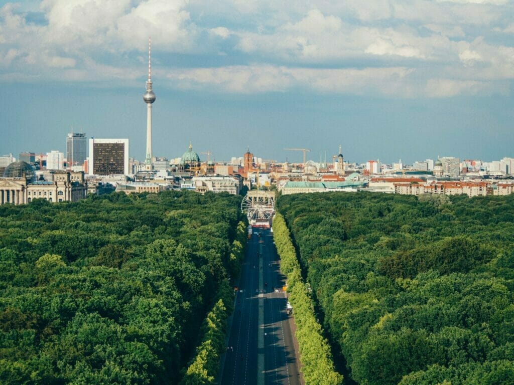 Das Bild zeigt Berlin im Sommer. Man sieht eine Straße, die Richtung Stadt führt. Links hinten erkennt man den Alex.
